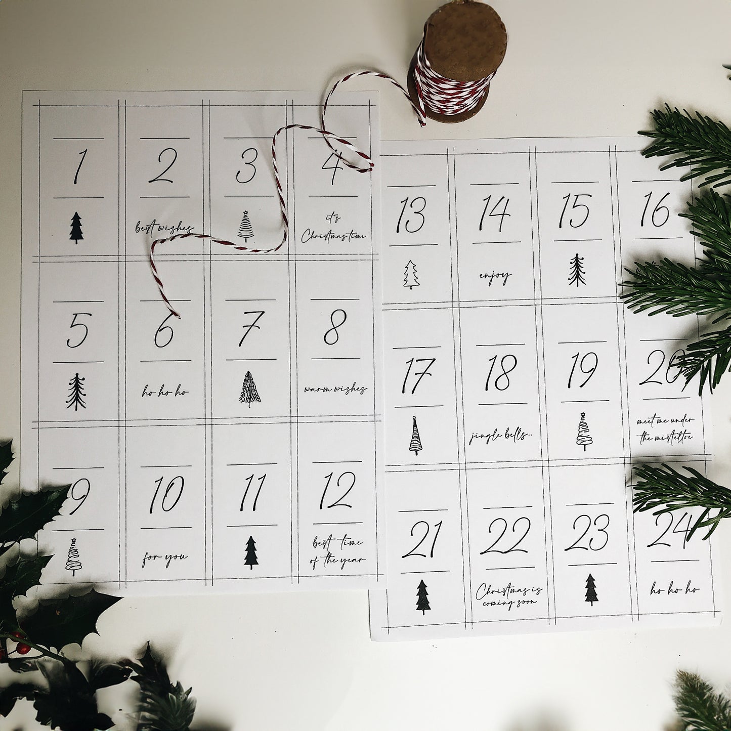 Minimalistische Adventskalender-Zahlen auf zwei Bögen Papier mit stilvoller Typografie und kleinen Weihnachtsillustrationen. Im Hintergrund liegen Tannenzweige und rot-weißes Geschenkband – perfekt für DIY-Adventskalender.