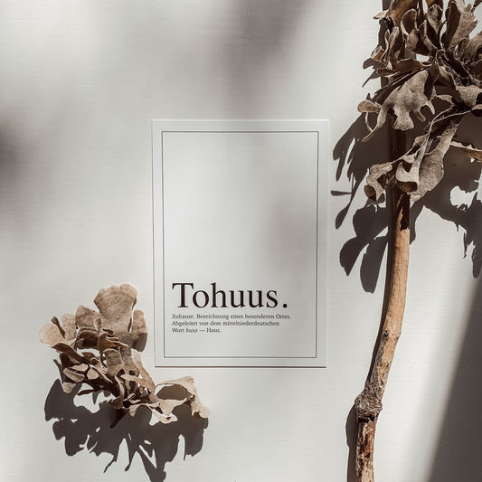 Minimalistische Postkarte mit dem Wort „Tohuus.“ und einer Definition in schwarzer Schrift auf weißem Hintergrund, fotografiert mit weichen Schatten.