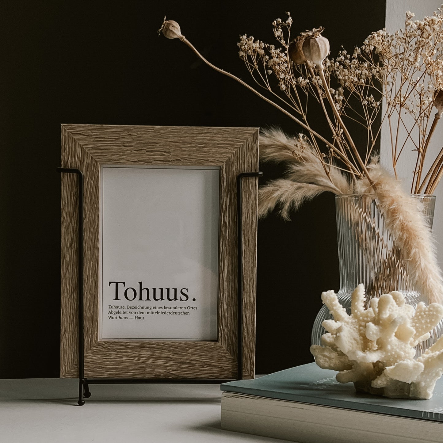 Postkarte mit dem Wort „Tohuus.“ in einem rustikalen Holzrahmen, dekoriert mit Muscheln und Trockenblumen.