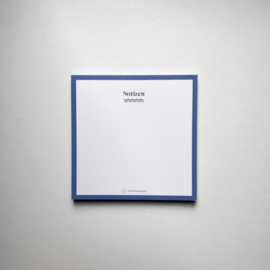 Quadratischer Notizblock mit blauem Rand und der Aufschrift 'Notizen' in schwarzer Schrift, darunter eine wellenförmige Linie. Unten mittig das Logo und der Schriftzug 'saltwaterdesigns'. Hintergrund ist eine glatte, helle Oberfläche.