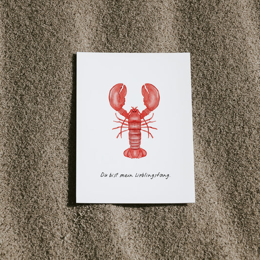 Postkarte Hummer von saltwaterdesigns liegend auf einem Sandstrand.