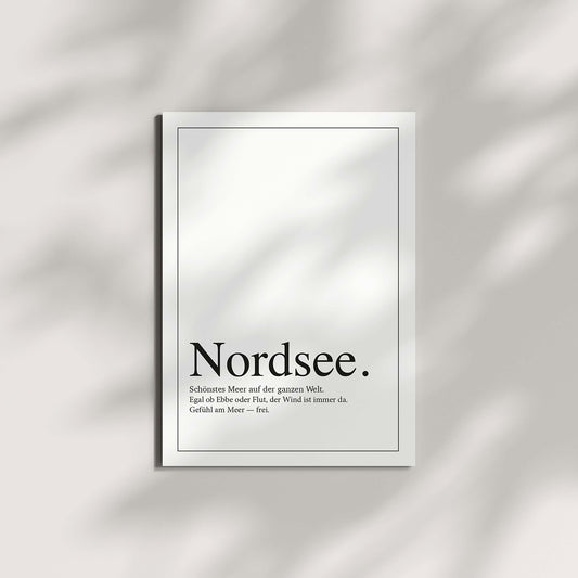 „Nordsee.“-Postkarte, auf einer hellen Oberfläche liegend. Weiche Schattenspiele von Zweigen oder Blättern fallen über die Karte.