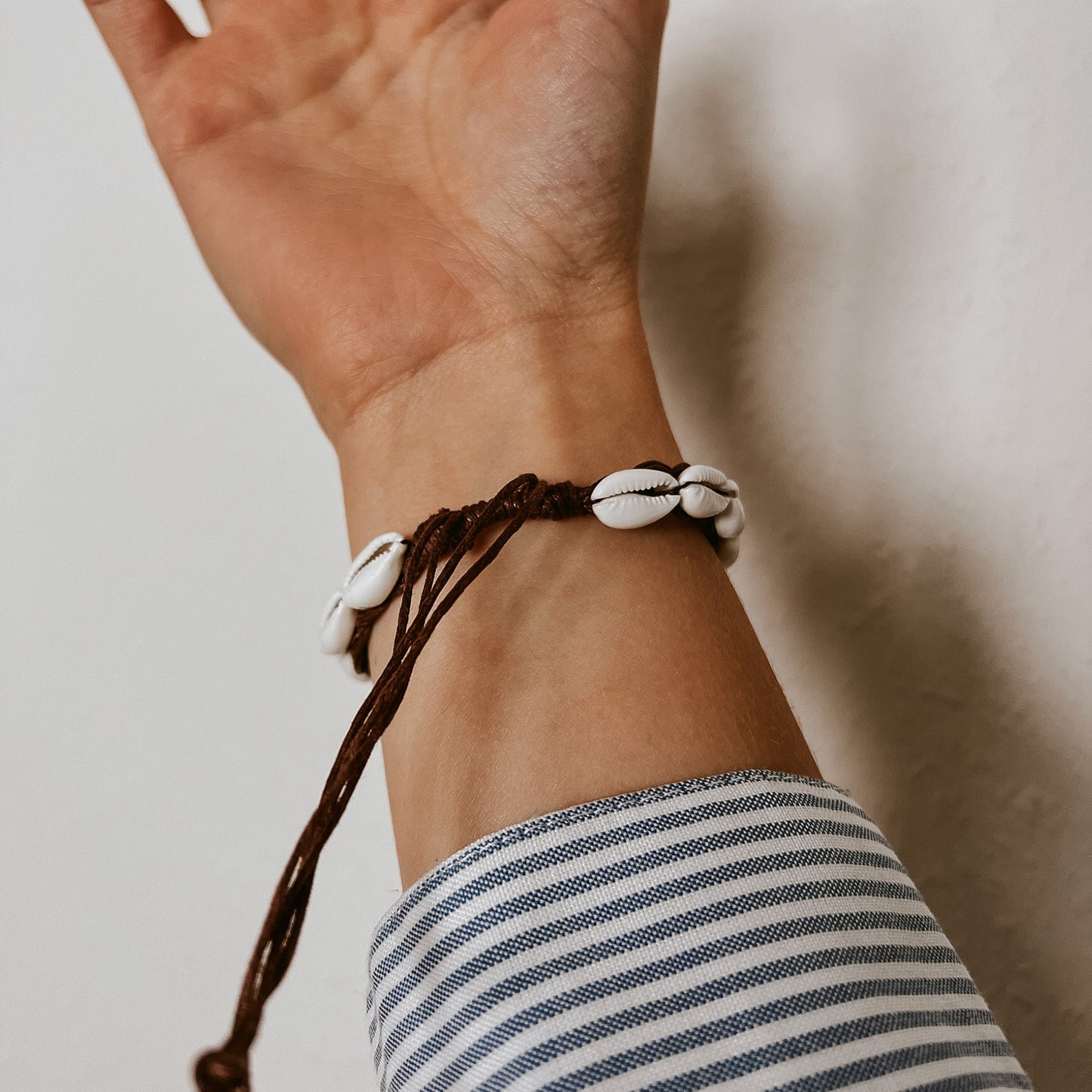 Kauri Muschelarmband auf dunkelbraunem, verstellbarem Band, getragen am Handgelenk, Detailansicht der Bänder. Schmuck von saltwaterdesigns.