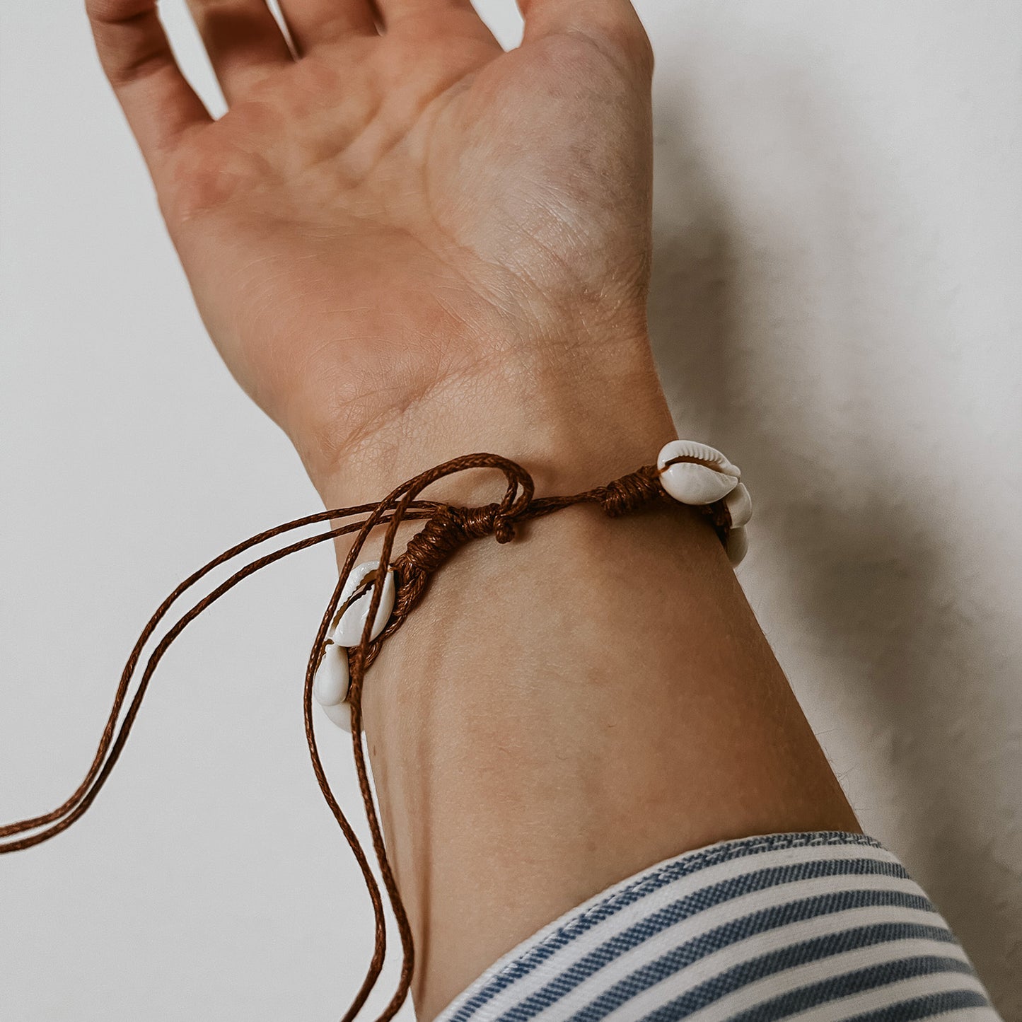 Muschelarmband Kauri mit hellbraunem, verstellbarem Band, getragen am Handgelenk, zeigt die Detailansicht vom Verschluss. Schmuck von der Marke saltwaterdesigns.