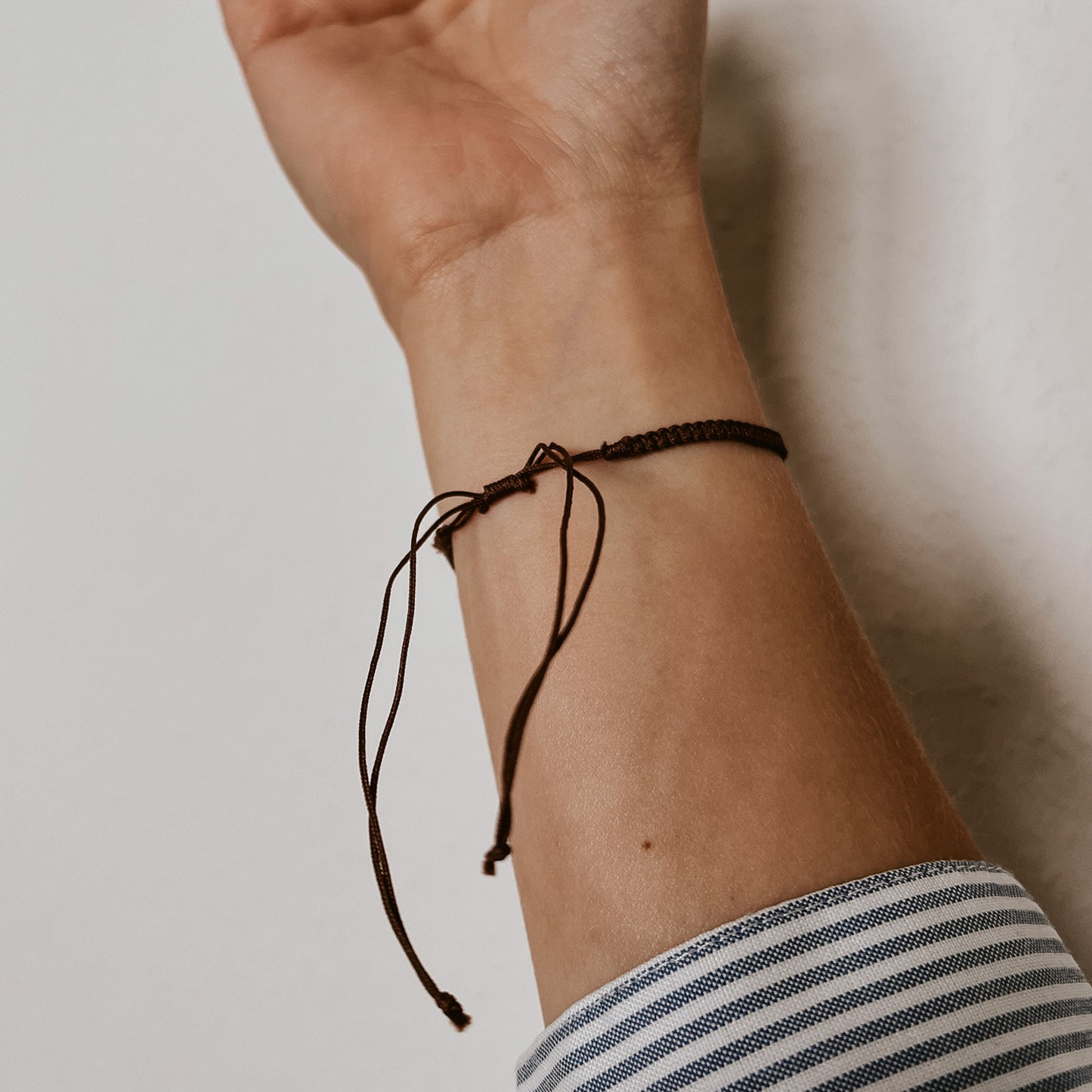 Rückansicht von dem braunen Bali Armband mit braunem Band und weißer Kauri Muschel. Der Verschluss ist verstellbar.