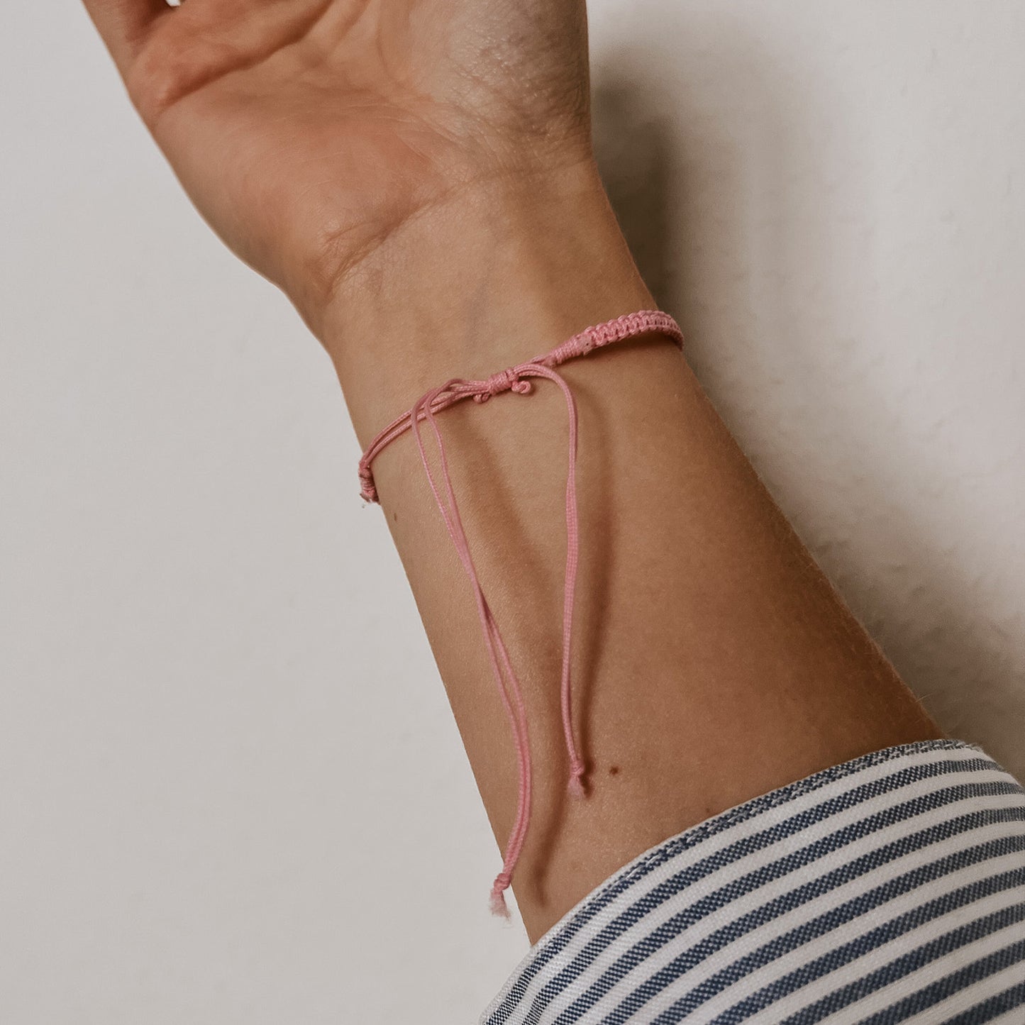 Rückansicht des rosa Bali Armbands mit rosa Band und weißer Kauri Muschel. Der Verschluss ist individuell verstellbar.