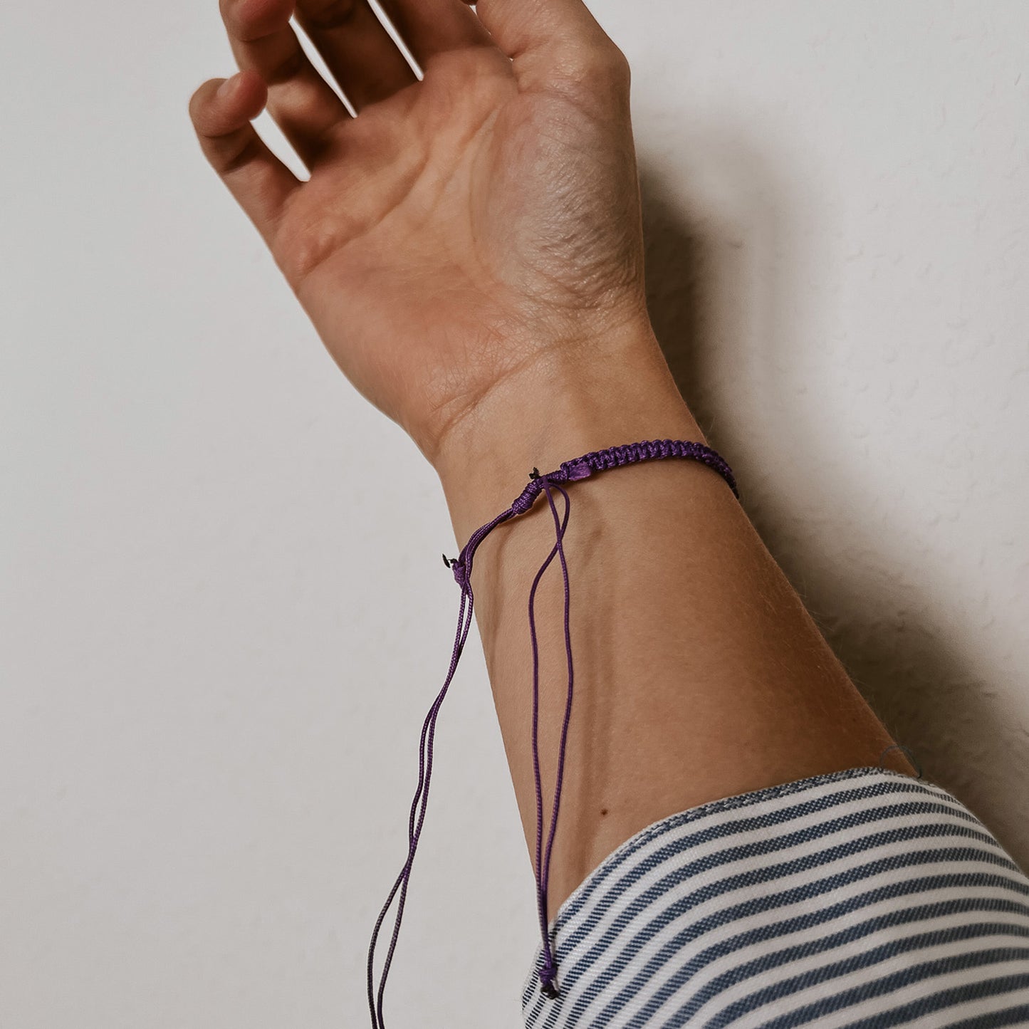 Rückansicht des lila Bali Armbands mit fein geflochtenem Band und einer weißen Kauri Muschel als Mittelpunkt. Der Verschluss ist verstellbar und sorgt dafür, dass sich das Armband angenehm und individuell an jedes Handgelenk anpassen lässt.