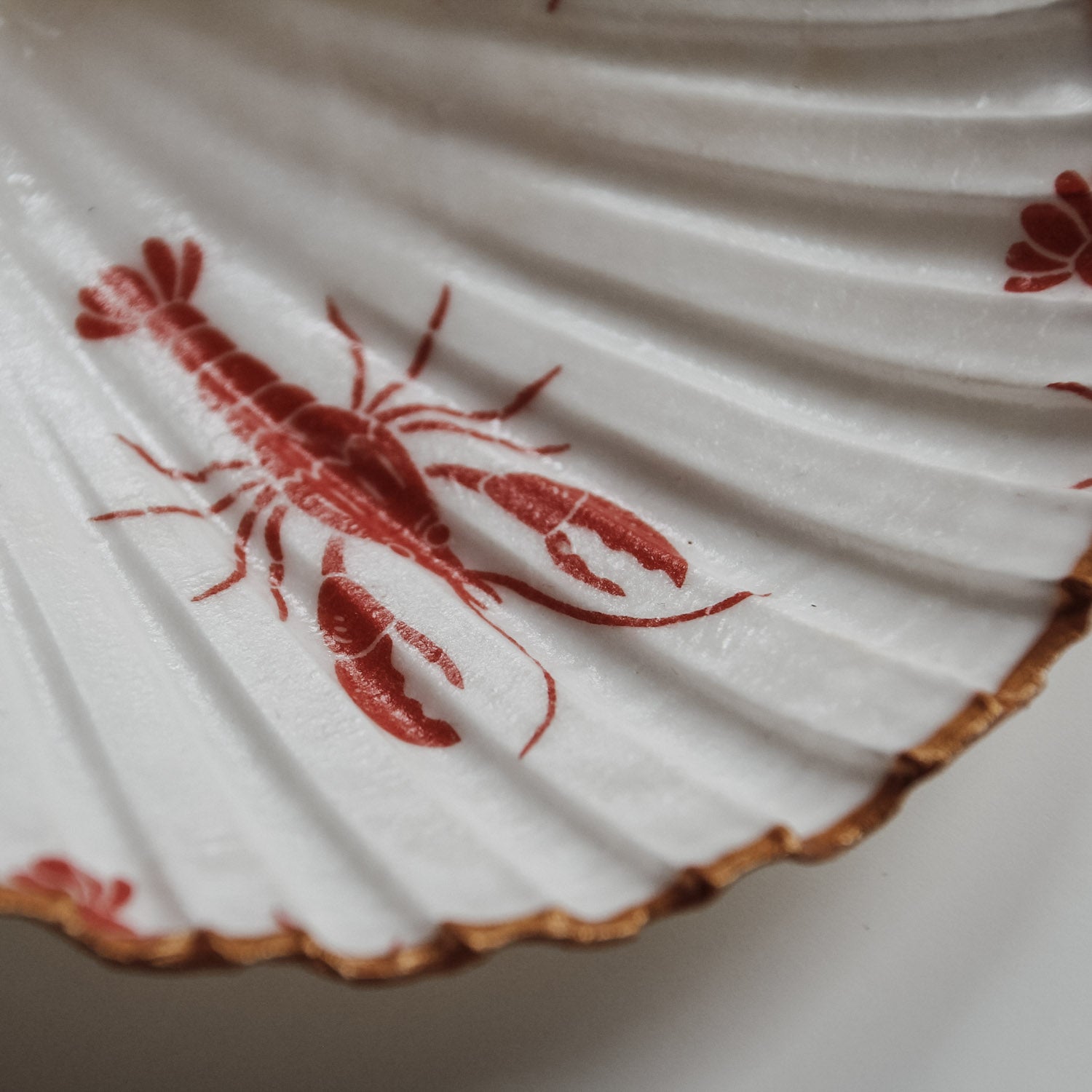 Detailaufnahme der Muschelschale mit rotem Hummer-Print und goldener Kante von saltwaterdesigns.