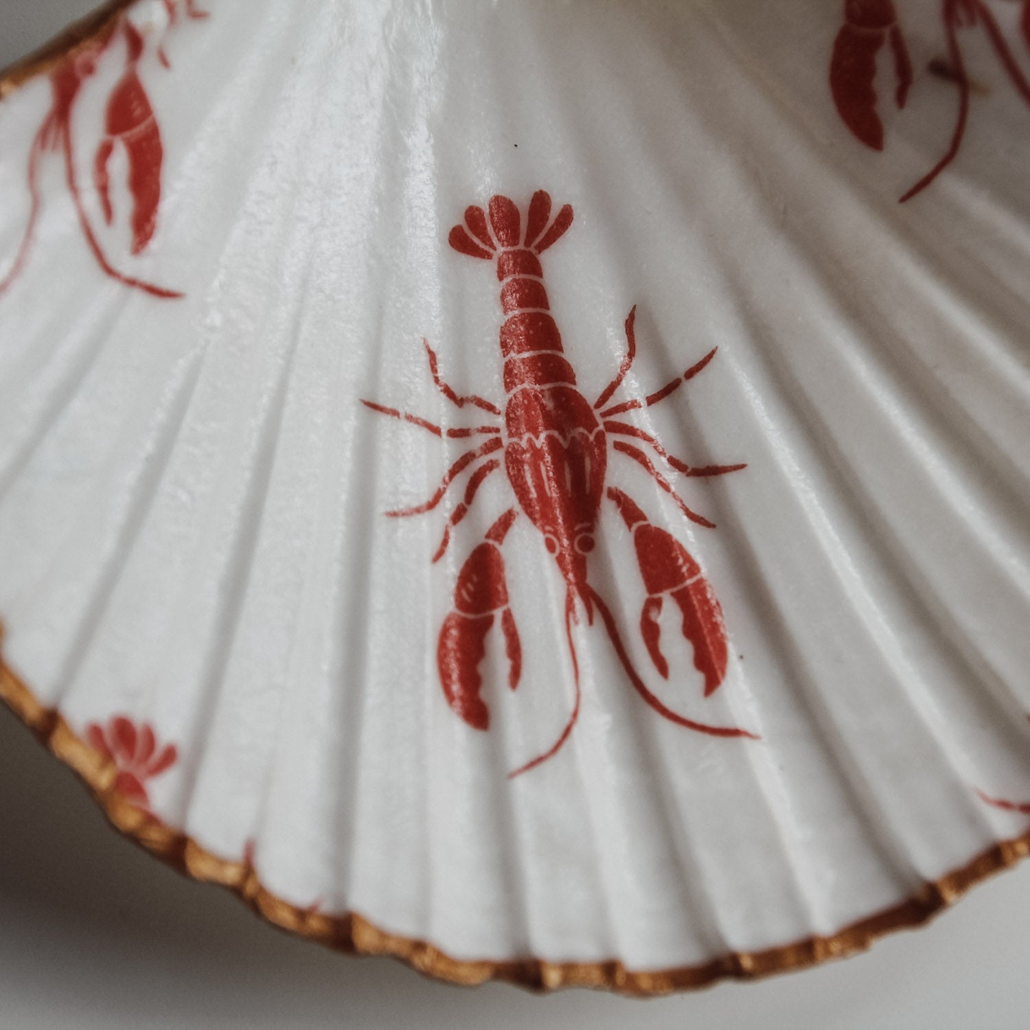 Detailaufnahme der Muschelschale mit rotem Hummer-Print, maritimes Design und goldener Kante von saltwaterdesigns.