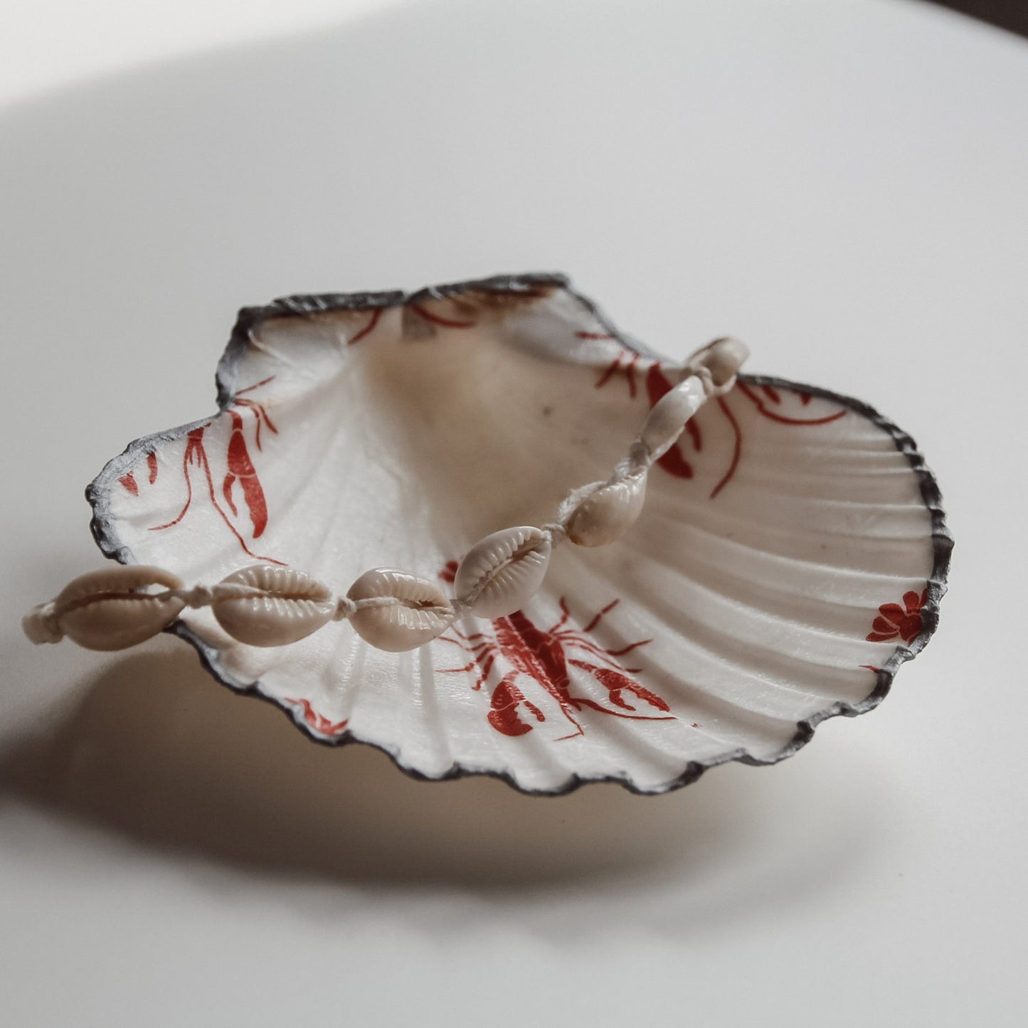 Dekorative Muschelschale mit rotem Lobster Design und silberfarbenem Rand, gefüllt mit einer Muschelkette. Handgemacht von saltwaterdesigns.