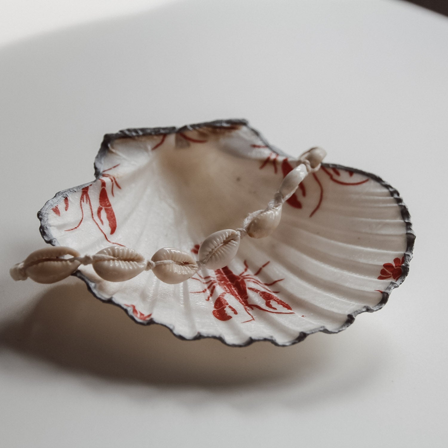 Dekorative Muschelschale mit rotem Lobster Design und silberfarbenem Rand, gefüllt mit einer Muschelkette. Handgemacht von saltwaterdesigns.
