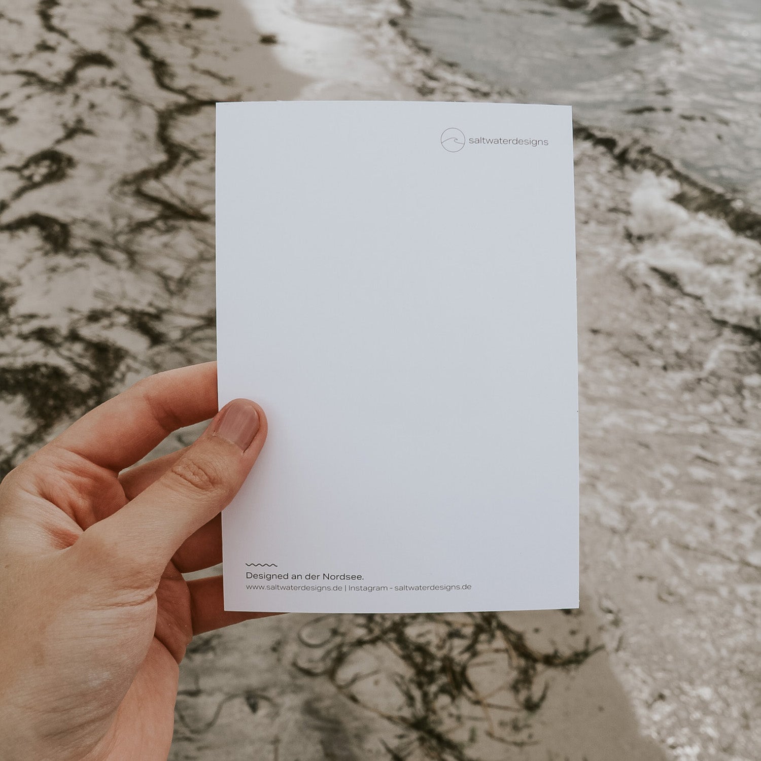 Rückseite der Postkarte mit Strandkorb-Motiv, in der Hand gehalten vor der Nordsee. Minimalistisches Design von Saltwater Designs, gestaltet an der Nordsee.
