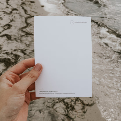 Rückseite der Postkarte mit Strandkorb-Motiv, in der Hand gehalten vor der Nordsee. Minimalistisches Design von Saltwater Designs, gestaltet an der Nordsee.