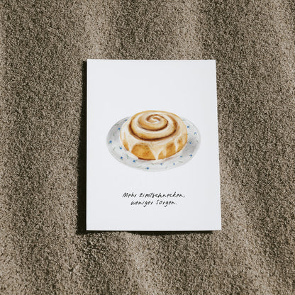 Postkarte Zimtschnecke von saltwaterdesigns liegend auf einem Sandstrand.