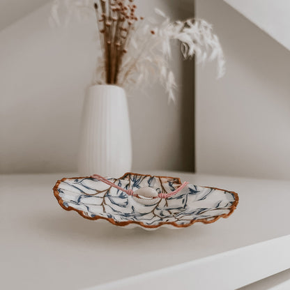 Zartes Ocean Kauri Muschelarmband in Rosa, dekorativ auf der Schmuckschale Muriwai von saltwaterdesigns präsentiert. Auf einem weißen Schrank arrangiert, mit Blumen im Hintergrund – ein elegantes Beispiel für stilvolle Wohn- und Dekoideen.