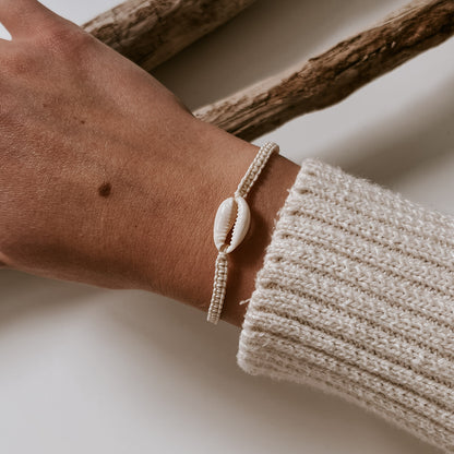 Weißes geflochtenes Armband mit einer weißen Kauri Muschel versehen, wird am Handgelenk getragen. Muschelarmband von saltwaterdesigns.
