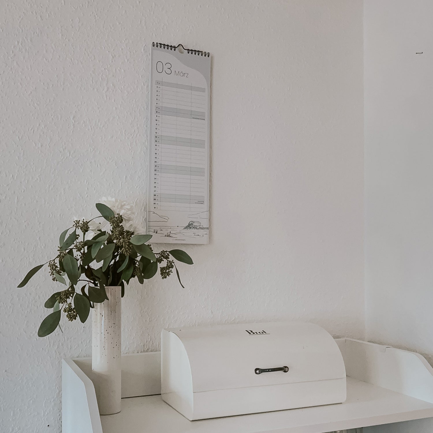 Aufnahme des schmalen Kalender 2026 in der Küche über einem Brotfach. Schlichter Hingucker mit liebevoll gemalten Illustrationen von der Nordseeküste.