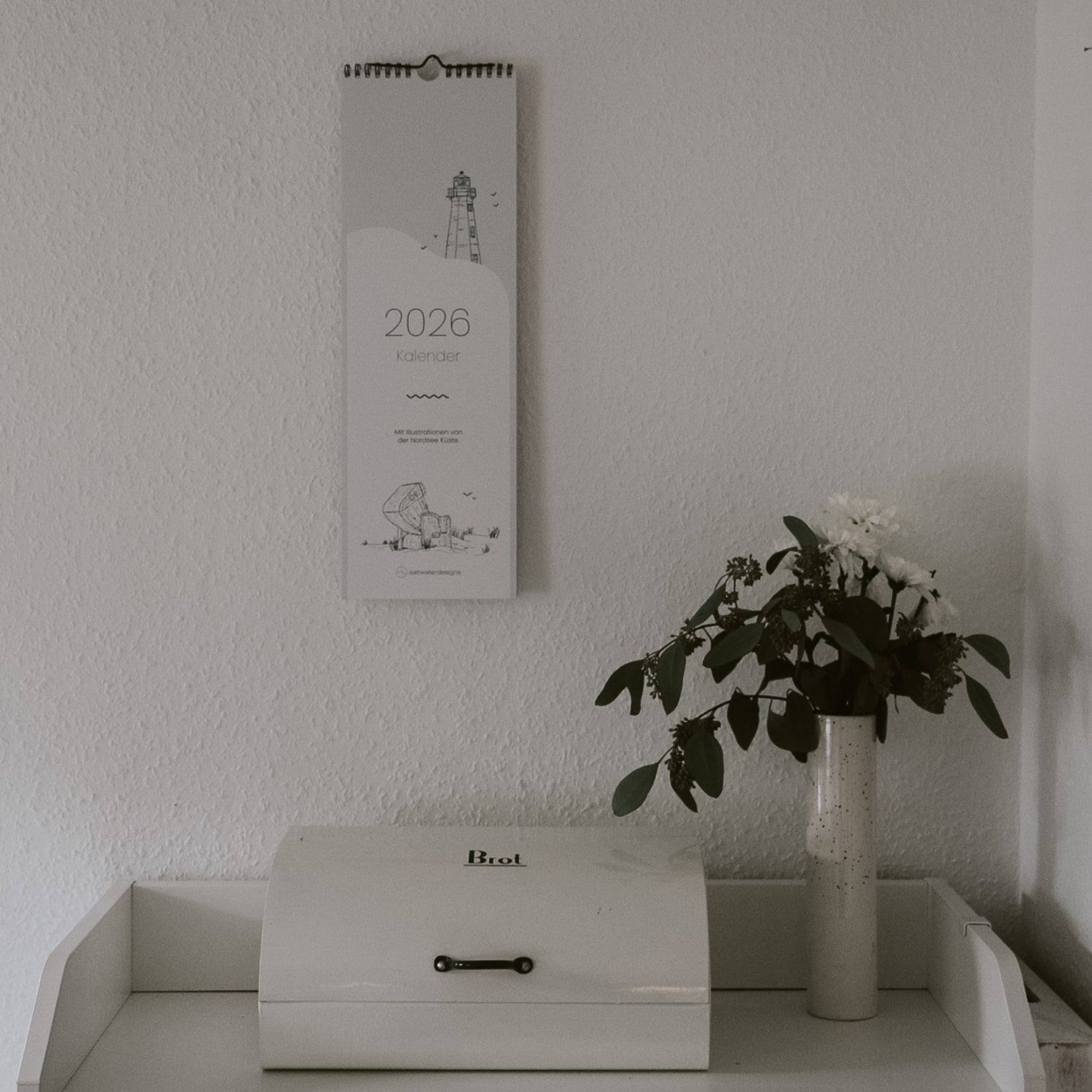 Kalender für Paare oder Singles hängt über Küchen Kommode. 13 Seiten für das Jahr 2026 mit Nordsee Illustrationen.