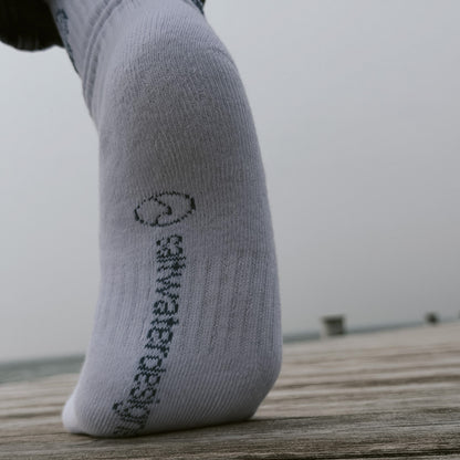 Saltwater Socken auf einem Holzsteg mit Meerblick, saltwaterdesigns Branding auf der Sohle, unterm Fuß, sichtbar.