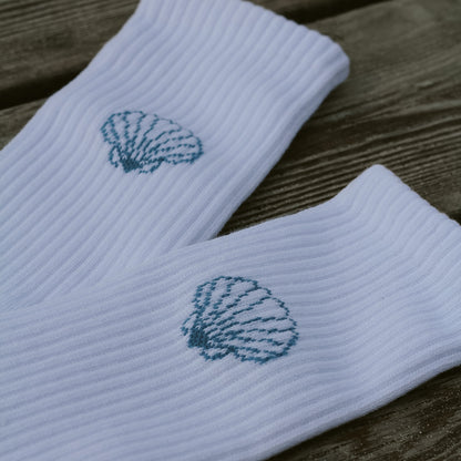 Detailaufnahme beider weißer Saltwater Socken mit eingestricktem Jakobsmuschel-Motiv auf Holzuntergrund.