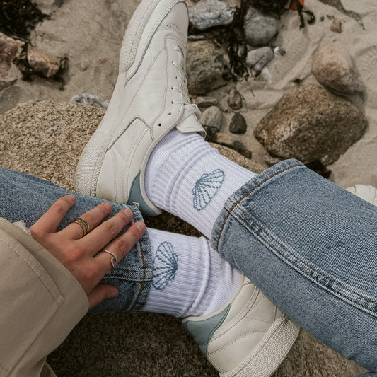 Saltwater Socken Muschel getragen zu Jeans und weißen Sneakern, Vogelperspektive auf Steinstrand. Tennissocken von saltwaterdesigns.